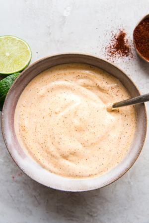 bowl of creamy chipotle mayonnaise with chipotle powder on the side and sliced limes