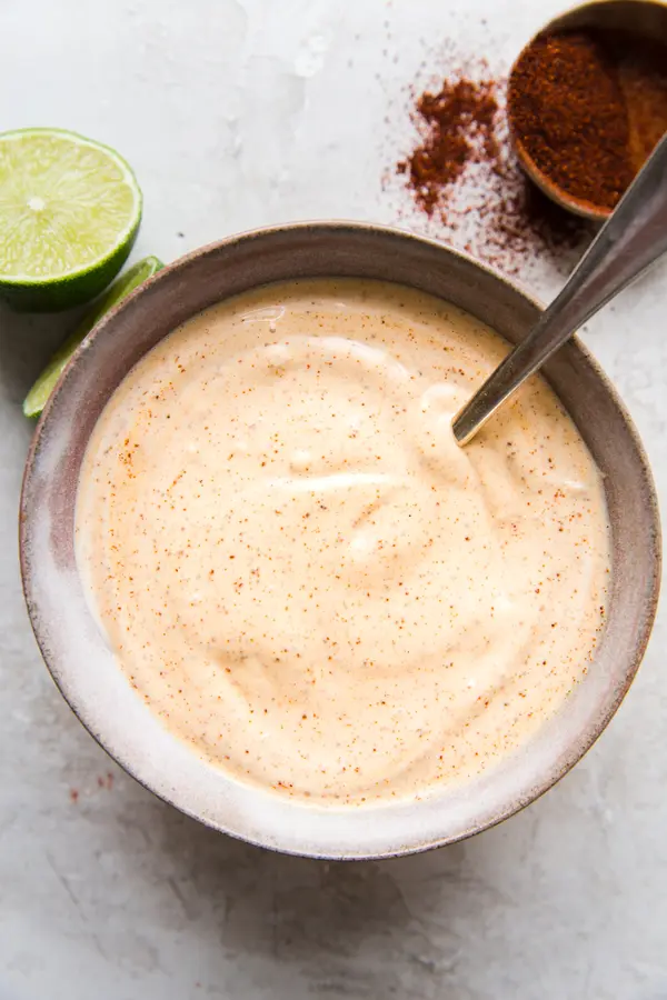 bowl of creamy chipotle mayonnaise with chipotle powder on the side and sliced limes