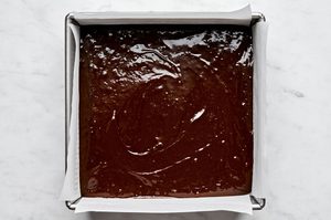 fudgy brownie batter in a greased ad parchment line 8x8 baking dish ready to be baked in the oven