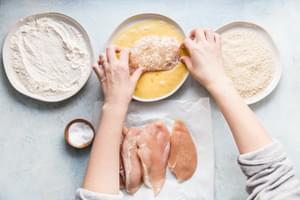 raw chicken being dipped in beaten eggs after being dipped in flour for crispy panko chicken