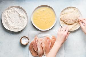 raw chicken being dipped in panko bread crumbs after being dipped in beaten eggs for crispy panko chicken