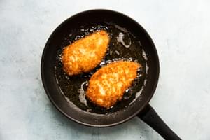 crispy panko chicken in a black skillet of sizzling oil
