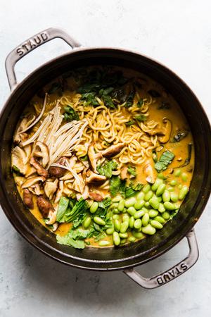 Soup pot full of vegetarian coconut curry ramen with mushrooms, bok choy, edamame