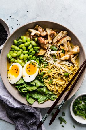 Bowl of vegetarian coconut curry ramen with mushrooms, bok choy, edamame and soft boiled egg with chopsticks