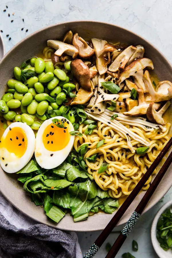 Bowl of vegetarian coconut curry ramen with mushrooms, bok choy, edamame and soft boiled egg with chopsticks