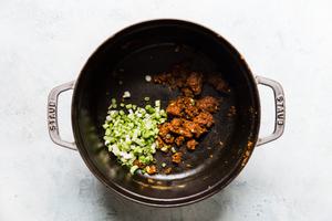 red curry paste and green onions in a soup pot for curry ramen