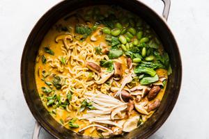 Pot of vegetarian coconut curry ramen with mushrooms, bok choy, edamame