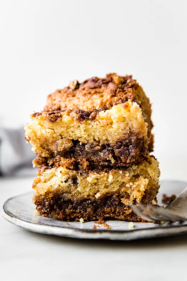 two slices of sour cream coffee stacked on a grey plate with a fork