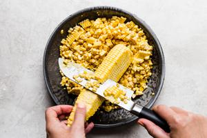 corn kernels being cut off the cob with a sharp knife into a pie pan