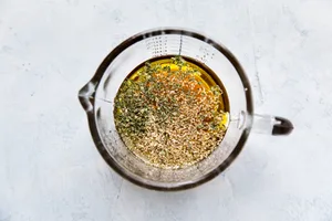 Italian salad dressing being made with olive oil, red wine vinegar, garlic powder, dried oregano & basil and salt
