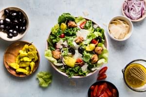 homemade Italian salad in a bowl surrounded by small bowls of parmesan cheese, red onions, black olives and tomatoes