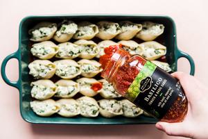marinara sauce being poured over pasta shells stuffed with ricotta, spinach, basil and ground chicken in a baking dish