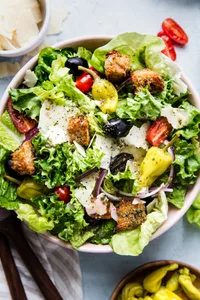 Italian Salad with romaine lettuce, croutons, tomatoes, pepperoncini, black olives, parmesan cheese and red onions in a bowl.