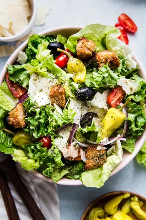 Italian Salad with romaine lettuce, croutons, tomatoes, pepperoncini, black olives, parmesan cheese and red onions in a bowl.
