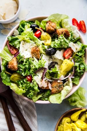 A simple Italian salad with romaine, red onion, Parm, peperoncini, olives, tomatoes, and homemade Italian dressing