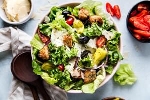 A simple Italian salad with romaine, red onion, Parm, peperoncini, olives, tomatoes, and homemade Italian dressing