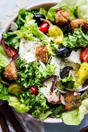A simple Italian salad with romaine, red onion, Parm, peperoncini, olives, tomatoes, and homemade Italian dressing