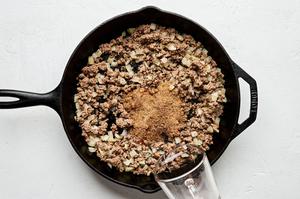 taco seasoning and water being added to a skillet with ground beef, garlic and onion