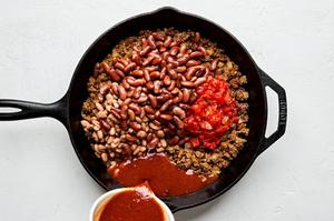 diced tomatoes, enchilada sauce, kidney beans, and pinto beans being added to a skillet with cooked taco meat