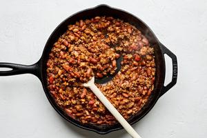 taco meat, diced tomatoes, enchilada sauce, kidney beans, and pinto beans being stirred in a skillet
