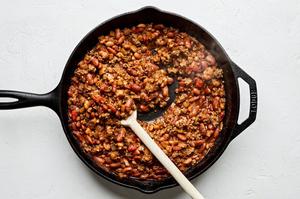 taco meat, diced tomatoes, enchilada sauce, kidney beans, and pinto beans being stirred in a skillet