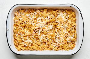 Fritos covered with mexican shredded cheese in the bottom of a baking dish