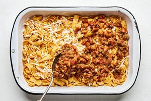ground beef and beans being spooned on top of Fritos and shredded cheese in a baking dish