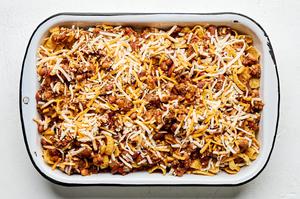 a baking dish of frito pie made with ground beef, kidney & pinto beans, cheese, enchilada sauce, tomatoes and taco seasoning