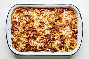 a baking dish of frito pie made with ground beef, kidney & pinto beans, cheese, enchilada sauce, tomatoes and taco seasoning