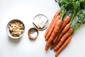 salted butter, brown sugar, salt and pepper in small bowls next to a bunch of carrots with stems on