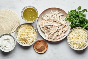 cheese, chicken, sour cream, green enchilada sauce, taco seasoning and cilantro in bowls for green chicken enchiladas