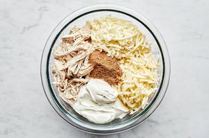 shredded chicken, shredded cheese, taco seasoning and sour cream in a bowl to make enchilada filling