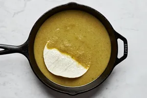 corn tortillas being dipped in green enchilada sauce in a skillet