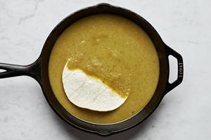 corn tortillas being dipped in green enchilada sauce in a skillet