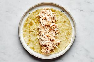a corn tortilla dipped in green enchilada sauce on a plate with chicken enchilada mixture on top