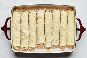 rolled green chicken enchiladas lined up in a casserole dish