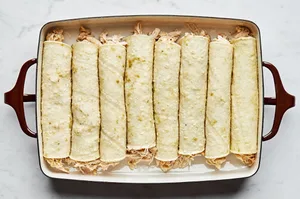 rolled green chicken enchiladas lined up in a casserole dish