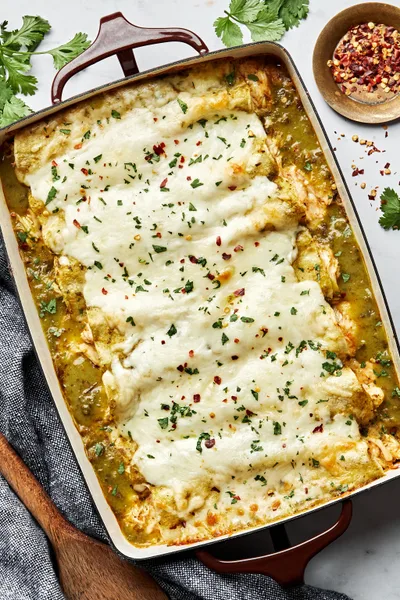 homemade green chicken enchiladas in a casserole dish made with chicken, cheese, sour cream and taco seasoning