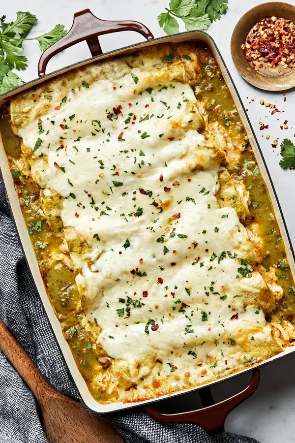 homemade green chicken enchiladas in a casserole dish made with chicken, cheese, sour cream and taco seasoning