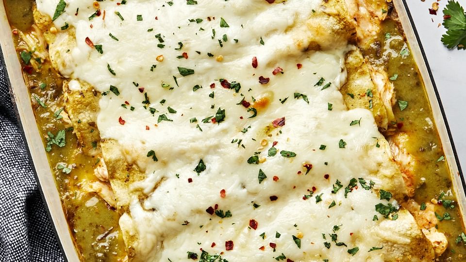 homemade green chicken enchiladas in a casserole dish made with chicken, cheese, sour cream and taco seasoning