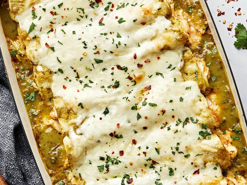homemade green chicken enchiladas in a casserole dish made with chicken, cheese, sour cream and taco seasoning