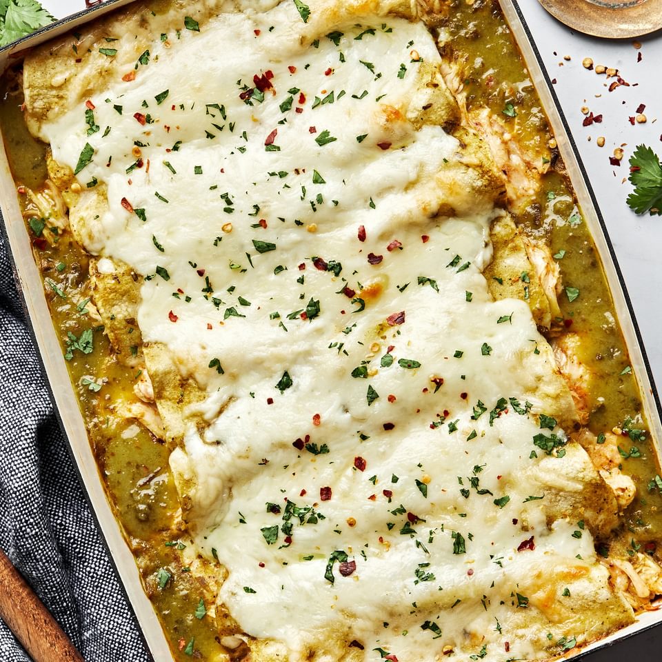 homemade green chicken enchiladas in a casserole dish made with chicken, cheese, sour cream and taco seasoning