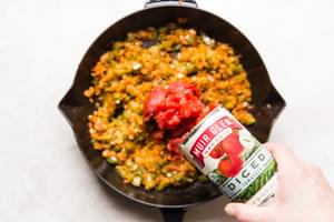 Muir Glen Tomatoes being added to onions, peppers and spices