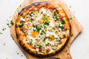 grilled shakshuka pizza on a wood pizza peel topped with fresh parsley and feta