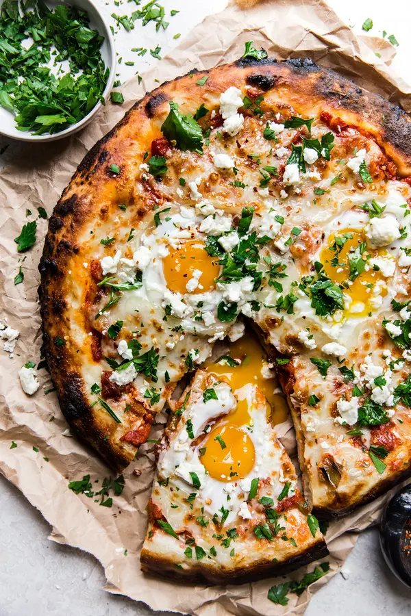 grilled shakshuka pizza with one slice out it and a side of finely chopped italian parsley