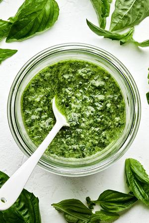 a jar of basil pesto with a spoon in it made with basil, Parmesan, pine nuts, cloves, sea salt and olive oil