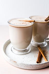 2 mugs of Hot Buttered Rum with cinnamon sticks on a plate