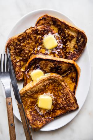4 slices of homemade French toast topped with sliced butter and syrup on a serving platter with a fork and a knife