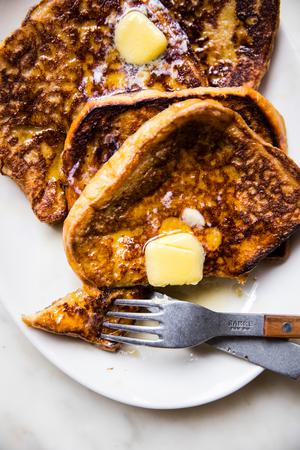 4 slices of homemade French toast topped with sliced butter and syrup on a plate with a fork and a knife and a bite being cut