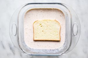 a slice of brioche bread being dipped cream and egg batter in a glass dish on the counter for homemade French toast